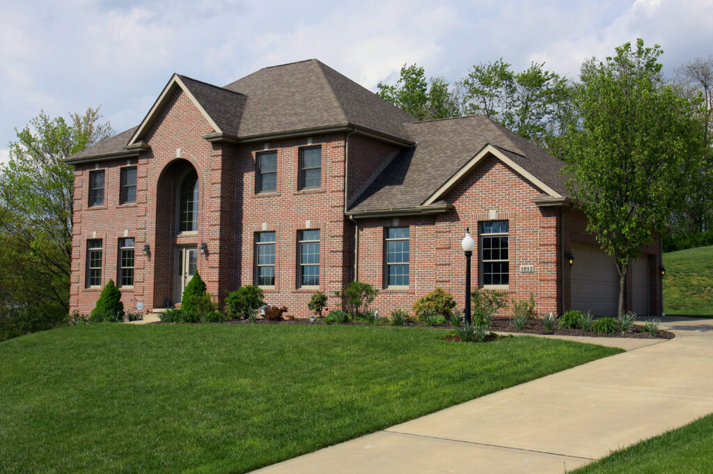 Large brick home with a landscaped front lawn before holiday lighting is installed